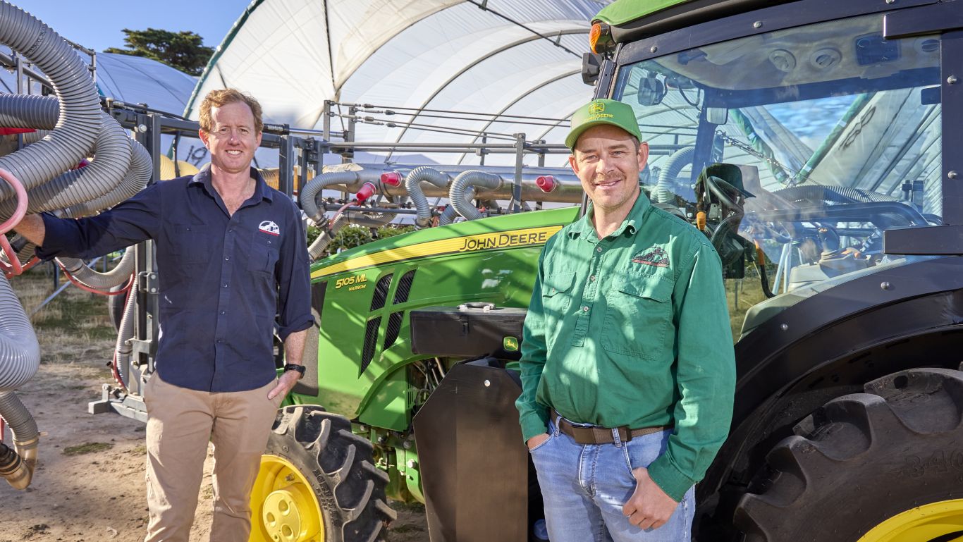 Two men beside a green John Deere tractor near tunnels