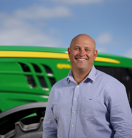 Smiling man stands in front of a tractor
