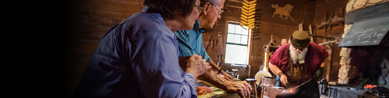 米国イリノイ州グランドデトゥールの史跡で、鍛冶屋が金属ハンマーを打つのを見る老夫婦