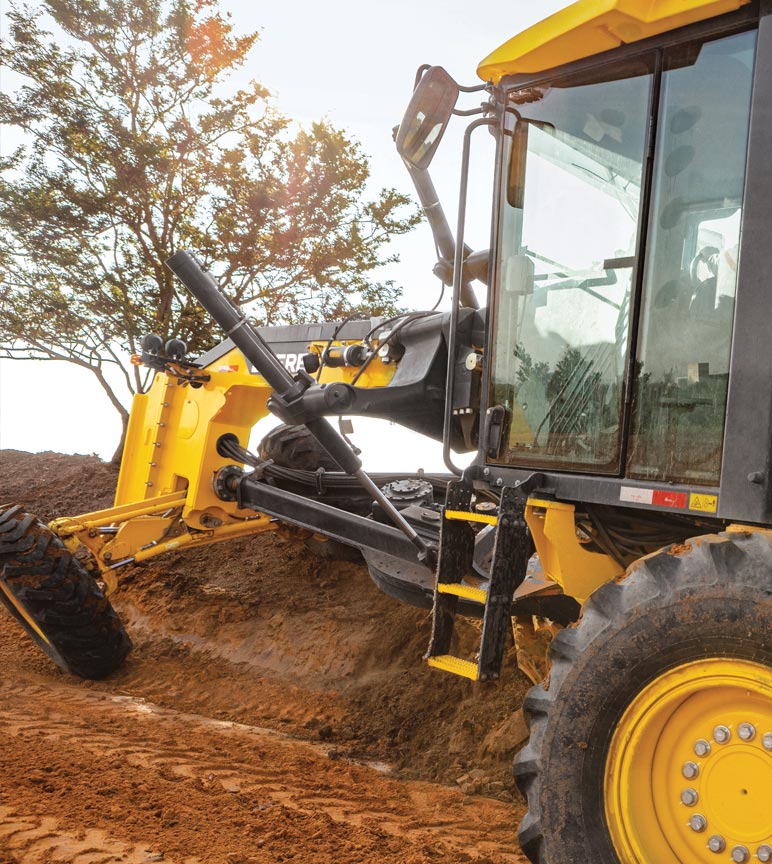 Yellow construction vehicle digging soil with a tree in the background.