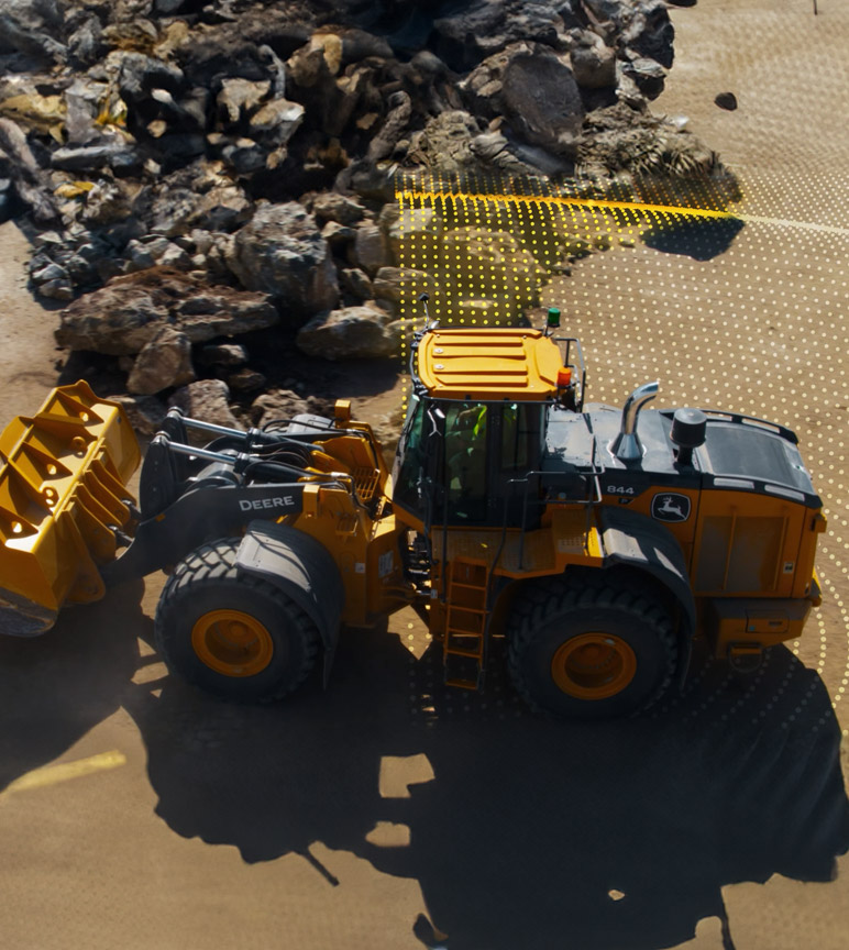 A large yellow John Deere 844 wheel loader moves rocks on a construction site, with a grid overlay showing its path.