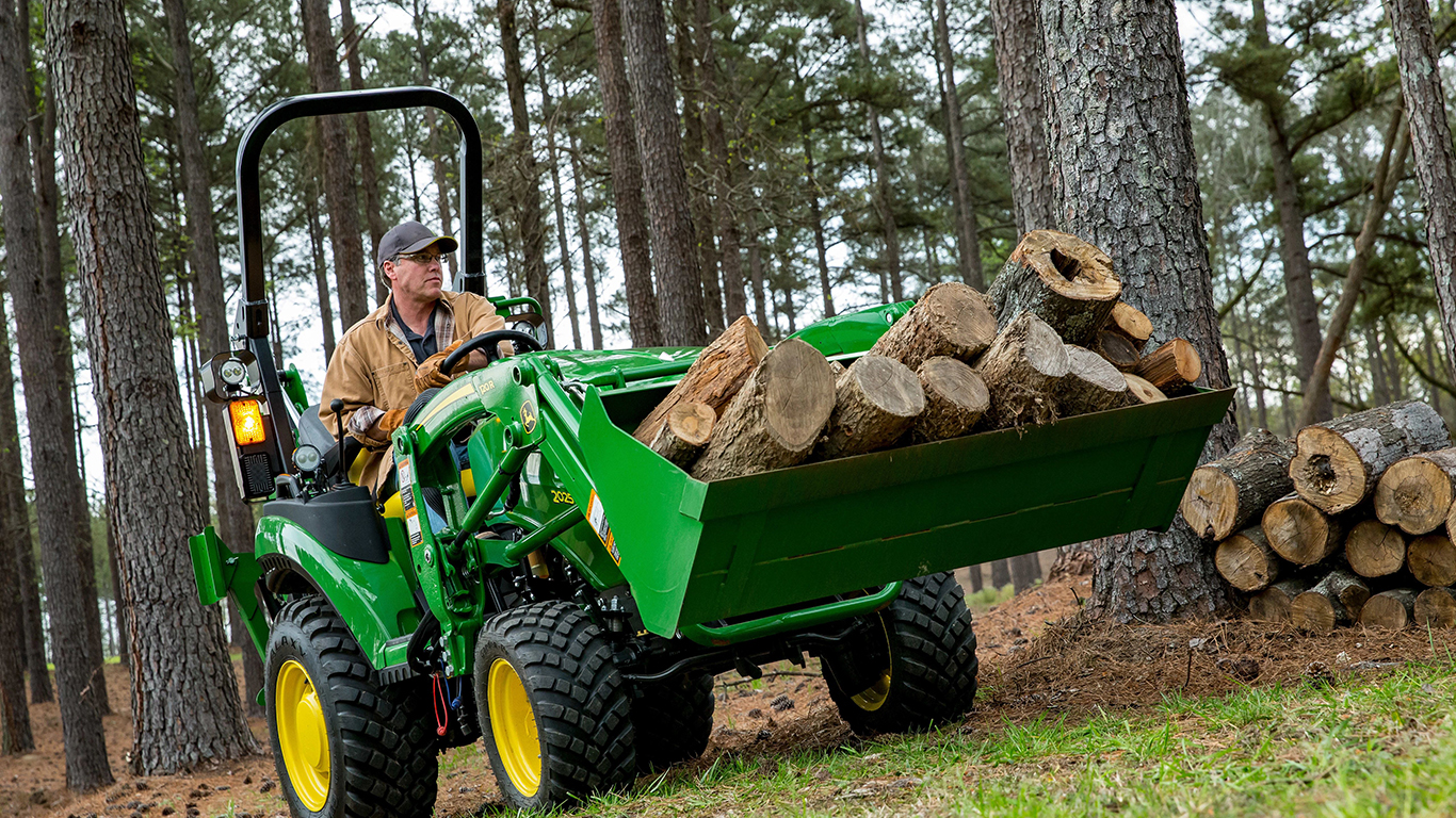 A person driving a tractor through forest hauling logs.
