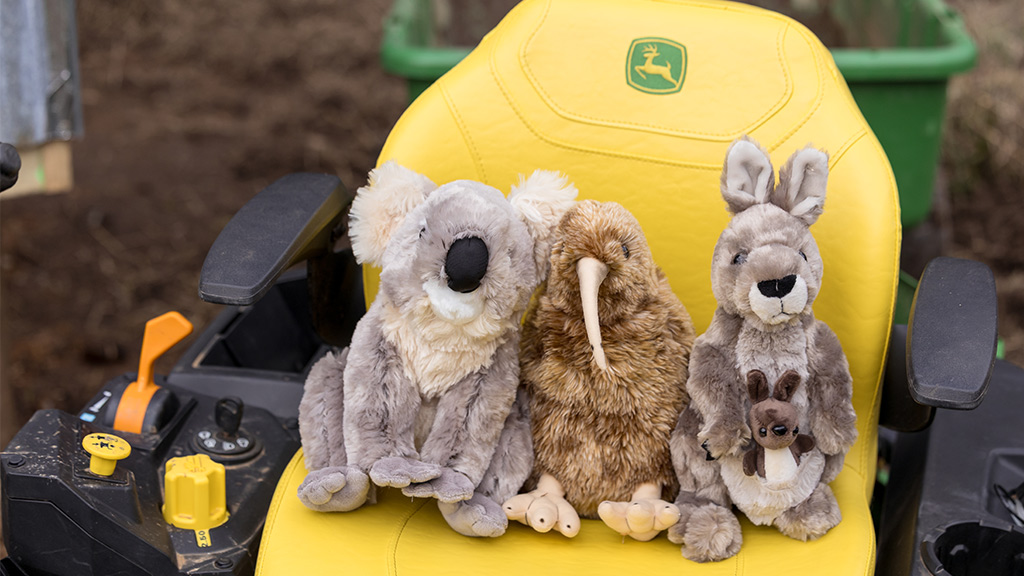 Three stuffed animals&mdash;koala, kiwi, and kangaroo&mdash;sit on yellow seat of John Deere tractor.