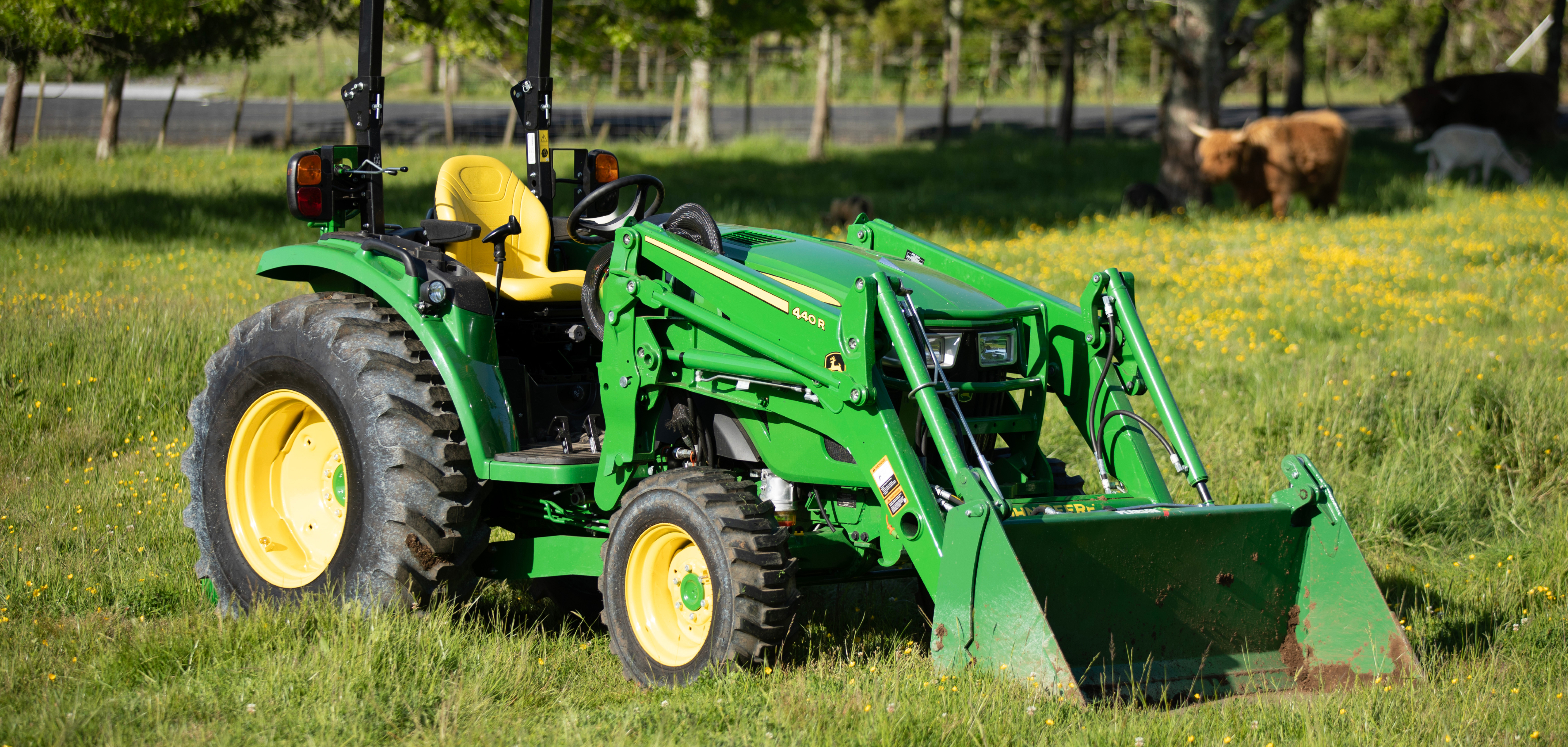 John Deere green tractor sitting on a field of grass with small yellow flowers and highland cows in the background