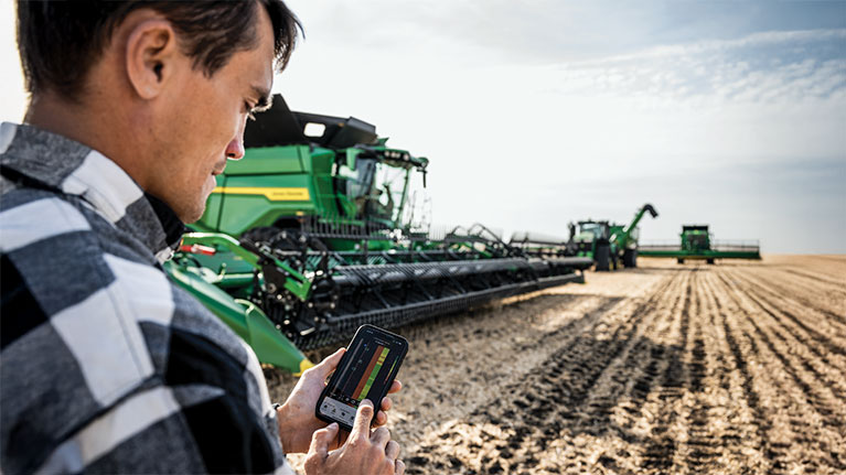 farmer using Connect Mobile in field with John Deere combine fleet