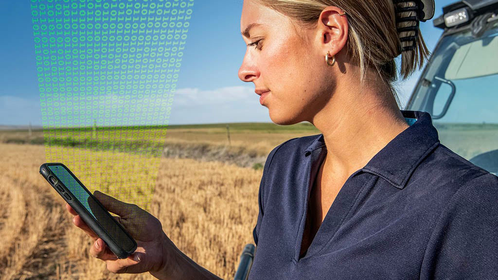 Close-up photo showing a female farmer consulting her mobile device while standing in a partially-harvested field. Close-up photo showing a female farmer consulting her mobile device while standing in a partially-harvested field.