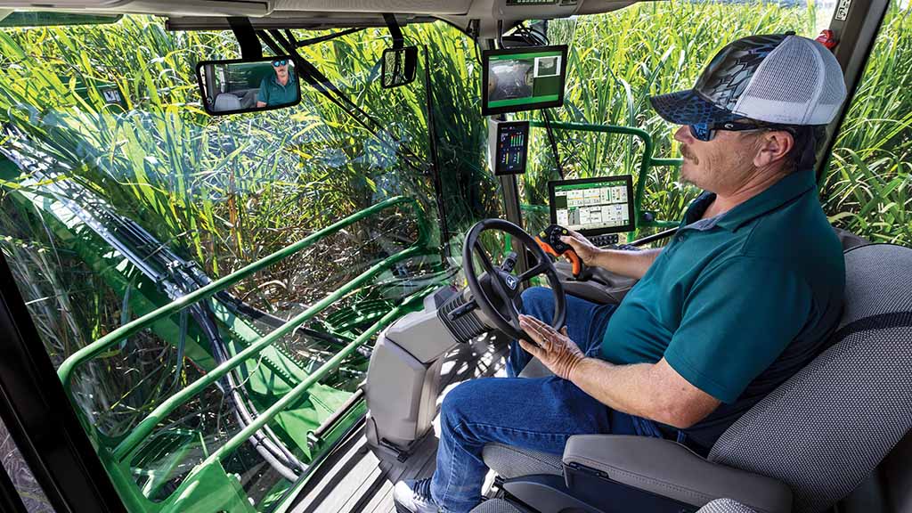 Close-up, in-cab photo showing a farmer operating a CH Series Sugar Harvester, with standing crop visibe throough the cab windows. Close-up, in-cab photo showing a farmer operating a CH Series Sugar Harvester, with standing crop visibe throough the cab windows.