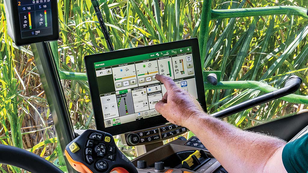 In-cab, close-up photo showing a farmer's arm and hand interacting with the G5 Display in a CH Series Sugar Harvesters. In-cab, close-up photo showing a farmer's arm and hand interacting with the G5 Display in a CH Series Sugar Harvesters.