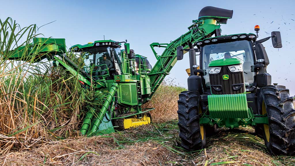 Front-view photo showing a CH Series Sugar Harvester unloading crop into a tractor-pulled grain cart. Front-view photo showing a CH Series Sugar Harvester unloading crop into a tractor-pulled grain cart.