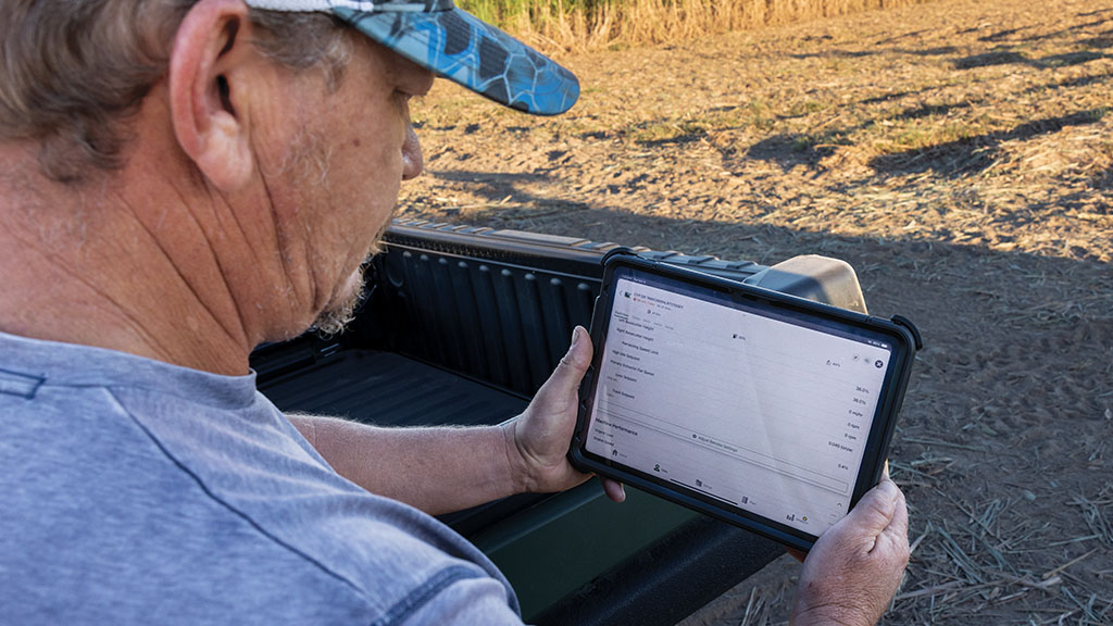 Close-up photo showing a farmer reviewing farm data on a tablet in a sugar cane field. Close-up photo showing a farmer reviewing farm data on a tablet in a sugar cane field.