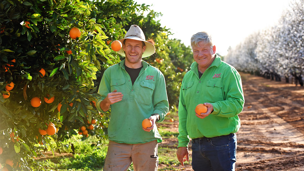 Darren and Garry Minter in an orange orchard holding oranges and smiling