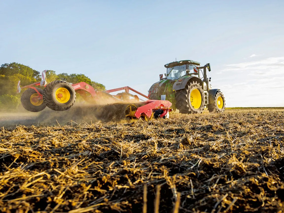 Stubble cultivation with John Deere tractor pulling red tillage implement, mixing soil and crop residue on harvested field